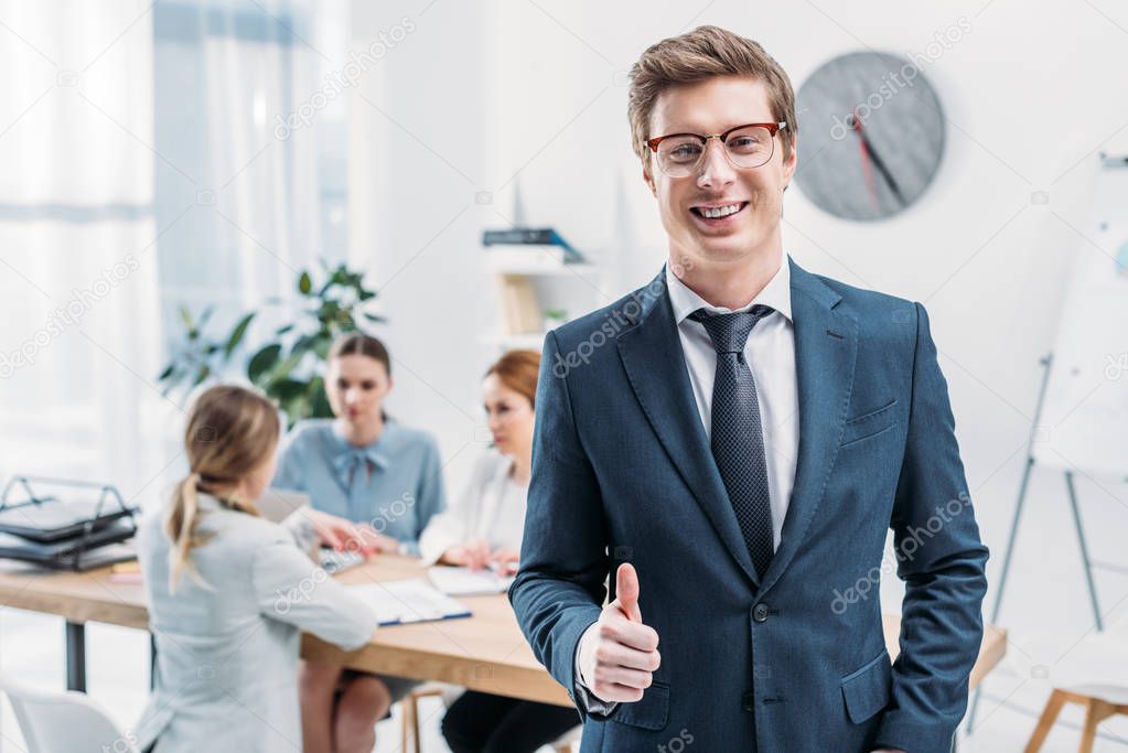 selective focus of cheerful recruiter in glasses showing thumb up near coworkers 