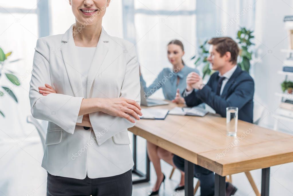 cropped view of cheerful recruiter standing with crossed arms near coworkers 