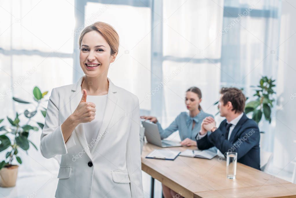 selective focus of happy recruiter showing thumb up near coworkers 