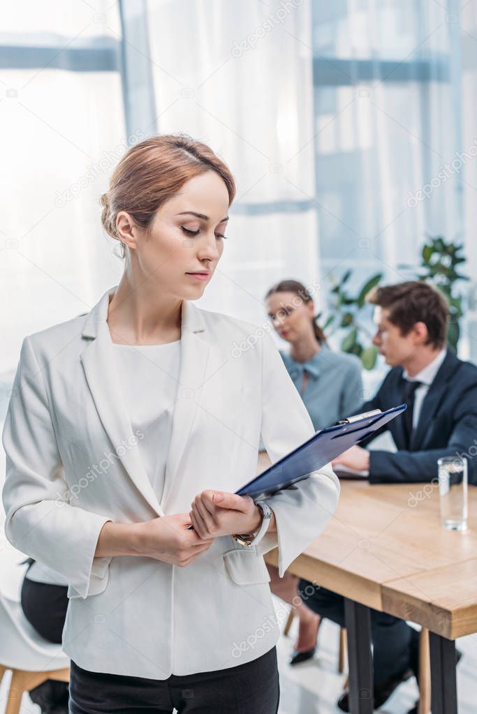 selective focus of attractive recruiter looking at clipboard near coworkers 