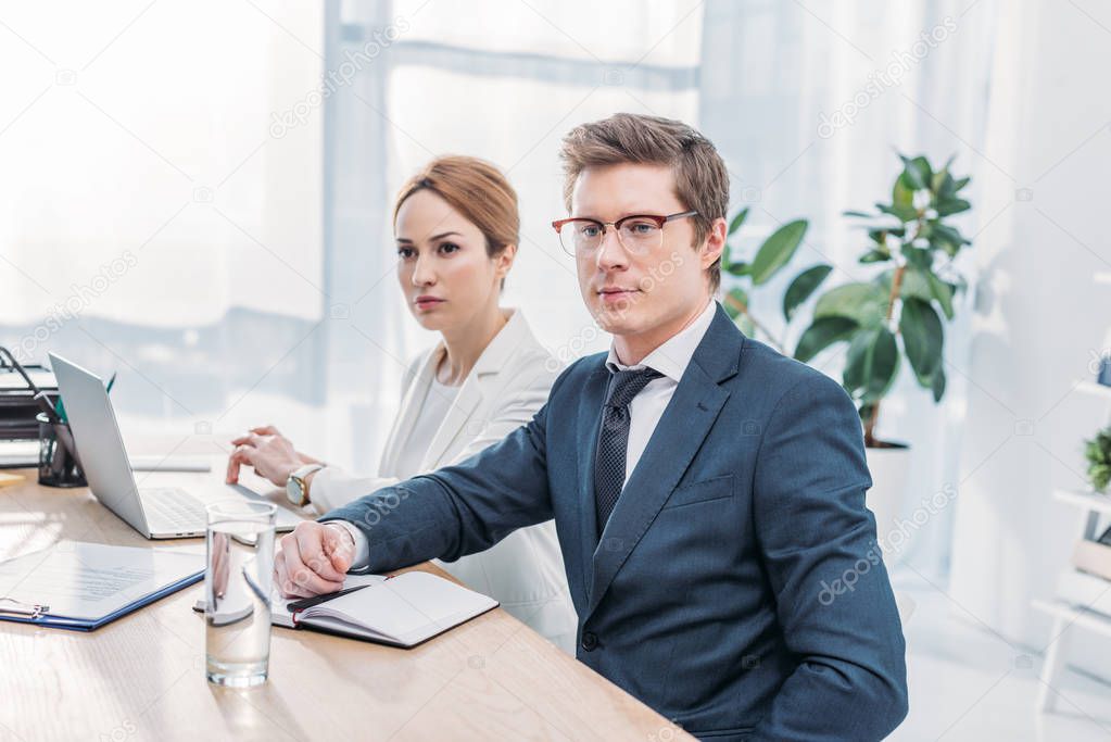 handsome recruiter in glasses sitting with attractive coworker in office 