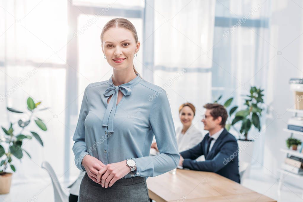 beautiful recruiter standing with clenched hands near coworkers in office 