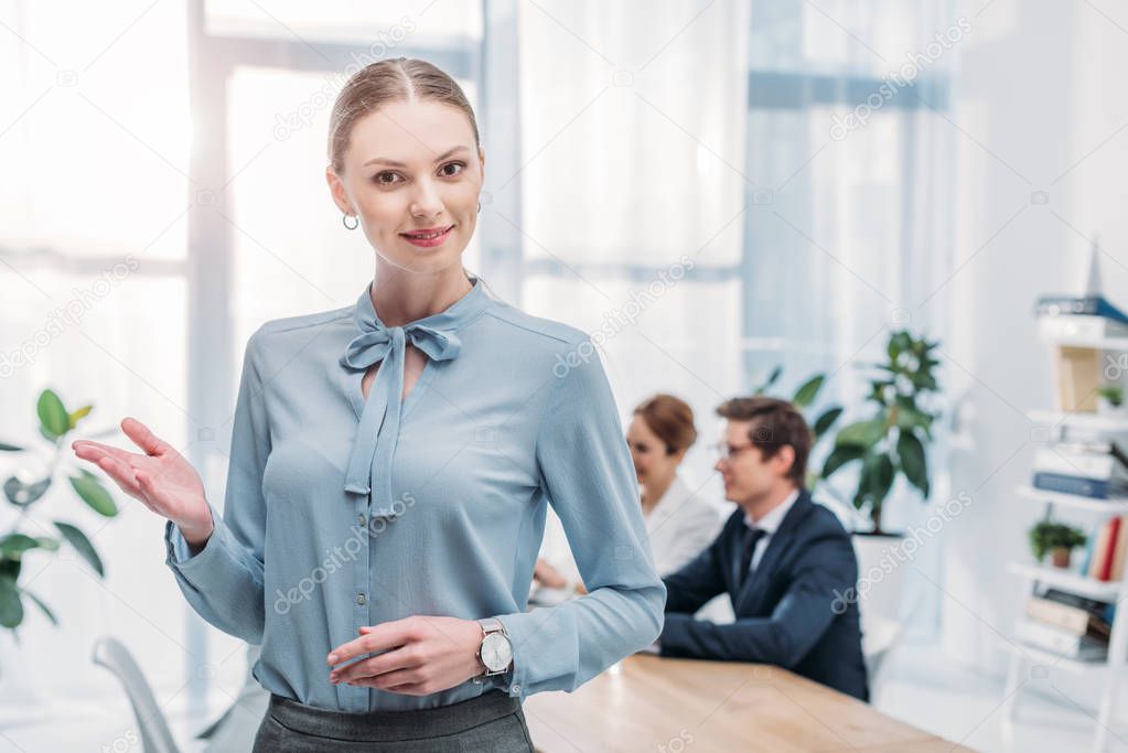 beautiful recruiter gesturing while standing near coworkers in office 