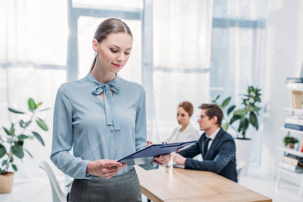 selective focus of attractive recruiter looking at clipboard near colleagues  
