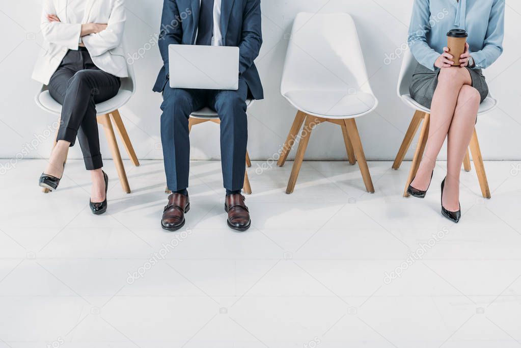 cropped view of women sitting with crossed legs and crossed arms near man using laptop 