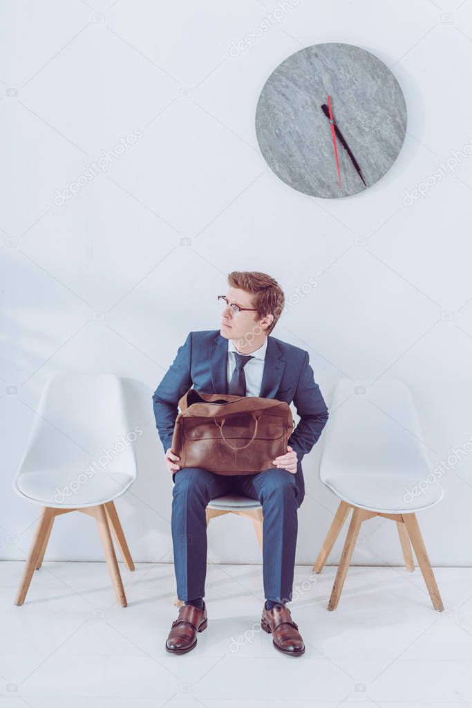 worried man in glasses holding briefcase while waiting job interview 