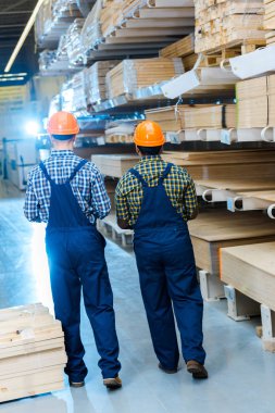 back view of two multicultural workers in overalls and helmets in warehouse clipart