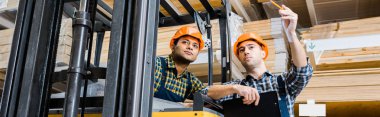 panoramic shot of warehouse worker pointing with pencil near indian colleague clipart
