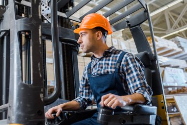 warehouse worker in uniform and helmet operating forklift machine clipart