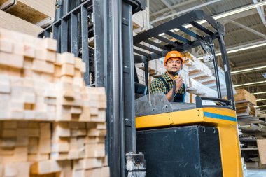 selective focus of indian warehouse worker sitting in forklift machine clipart