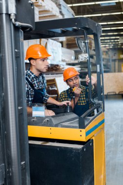 yakışıklı, dikkatli işçi kaskı içinde forklift makinede oturan Hint meslektaşım konuşan üzerinde walkie talkie