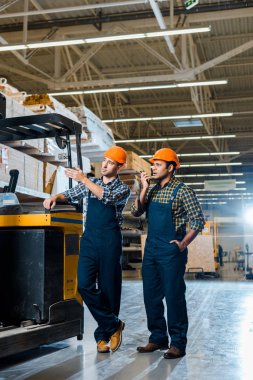 Forklift makinesi yakınında kask ve ekose gömlekler konsantre çok kültürlü işçiler