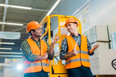 cheerful multicultural workers talking and gesturing while standing near scissor lift  clipart
