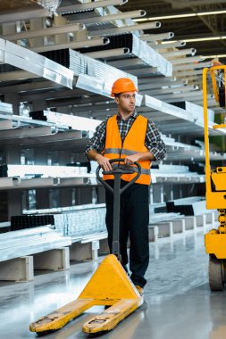 handsome, serious warehouse worker standing near pallet jack clipart