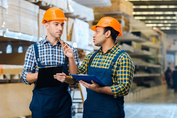 Two Serious Multicultural Warehouse Workers Talking Holding Clipboards — Stock Photo, Image
