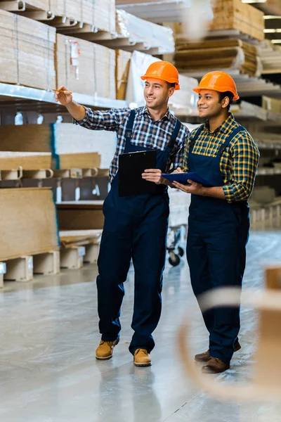 Smiling Warehouse Worker Uniform Pointing Finger Indian Colleague — Stock Photo, Image