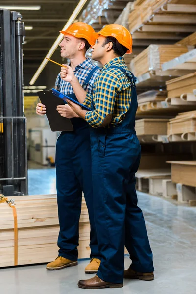 Two Multicultural Workers Uniform Holding Clipboards While Standing Warehouse — Stock Photo, Image