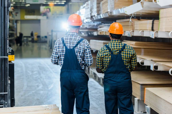 Back View Two Multicultural Workers Overalls Plaid Shirts Helmets Warehouse — Stock Photo, Image