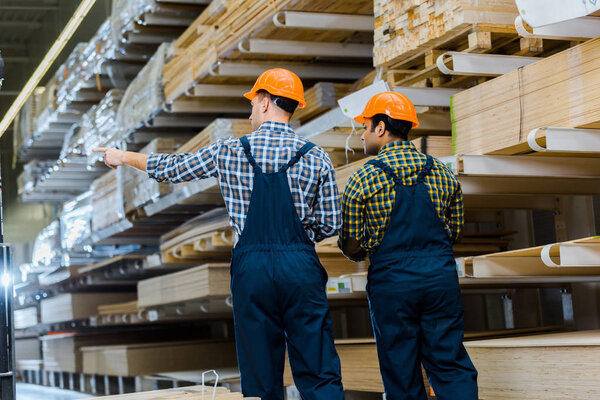 back view of two multicultural workers in uniform and safety vasts in storehouse