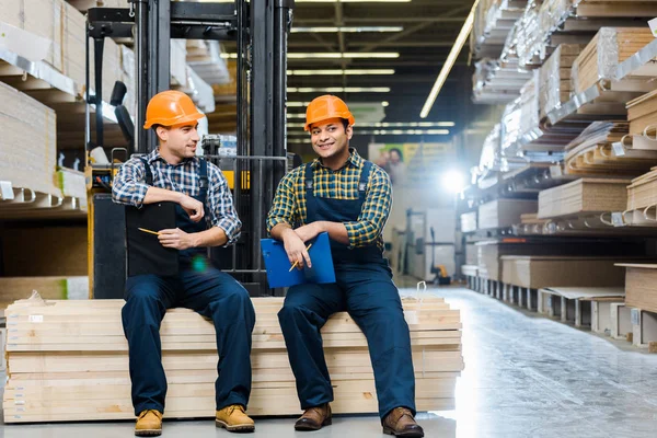 Two Smiling Multicultural Workers Clipboards Sitting Plywood — Stock Photo, Image