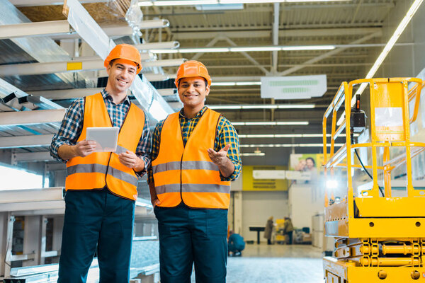 smiling multicultural workers in safety vasts and helmets looking at camera