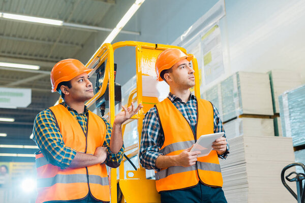 selective focus of multicultural workers looking away in warehouse