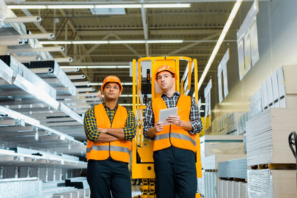 selective focus of serious multicultural workers standing near scissor lift