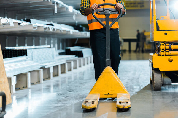 partial view of warehouse worker standing with pallet jack near scissor lift