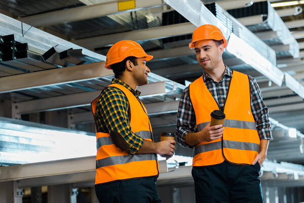 smiling multicultural workers holding paper cups while standing in warehouse