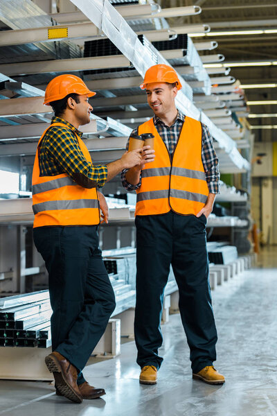 cheerful multicultural workers clinking with paper cups while standing in warehouse