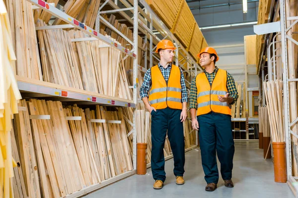 Uśmiechnięci Wielokulturowi Pracownicy Rozmawiający Podczas Chodzenia Wzdłuż Regałów Drewnianymi Materiałami — Zdjęcie stockowe