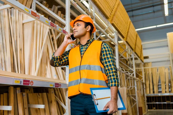 Handsome Indian Storehouse Worker Talking Smartphone Holding Clipboard — Stock Photo, Image