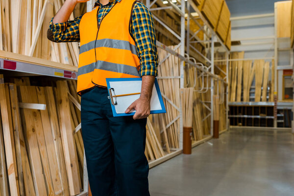 partial view of warehouse worker in safety vast holding clipboard