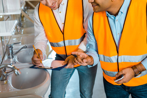 cropped view of multicultural colleagues in safety vests working in plumbing department
