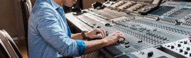 panoramic shot of mixed race sound producer working at mixing console in recording studio clipart