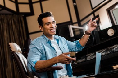 handsome cheerful mixed race sound producer gesturing while working in recording studio clipart