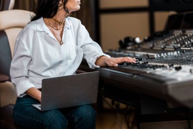 cropped view of sound producer working at mixing console and using laptop  clipart