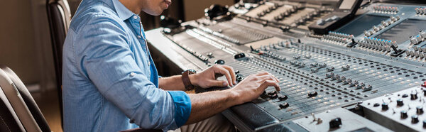 панорамный снимок продюсера смешанного расового звука, работающего на микширующей консоли в студии звукозаписи
