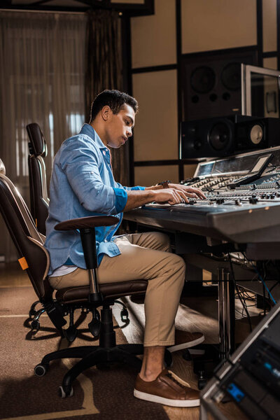 attentive mixed race sound producer working at mixing console in recording studio