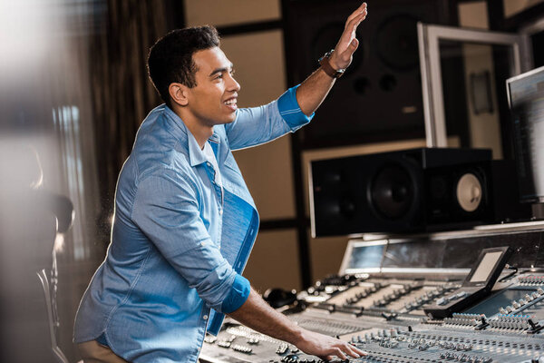 selective focus of smiling mixed race sound producer gesturing while working in recording studio
