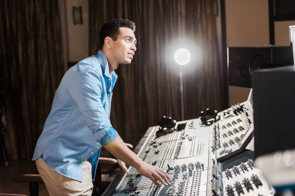 attentive mixed race sound producer working at mixing console in recording studio