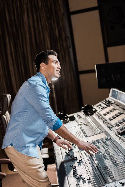 smiling mixed race musician working at mixing console in recording studio