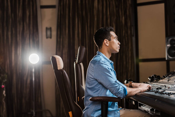 concentrated sound producer sitting in office chair and working at mixing console