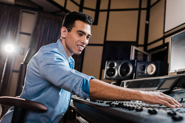 smiling mixed race sound producer working at mixing console in recording studio