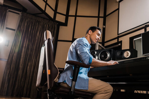 handsome mixed race sound producer working in recording studio at mixing console