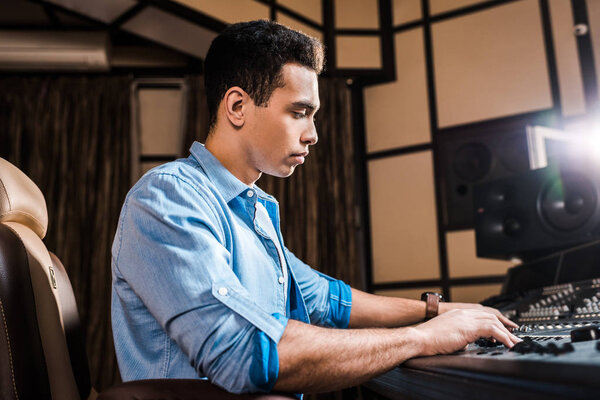 concentrated mixed race sound producer working at mixing console in recording studio
