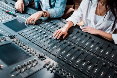 cropped view of two multicultural sound producers working at mixing console in recording studio clipart