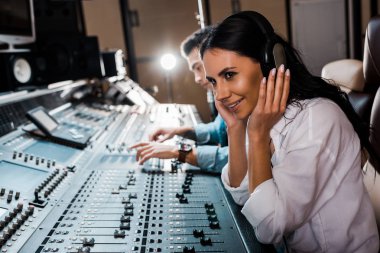  sound producer in headphones near mixed racial friend working at mixing console clipart