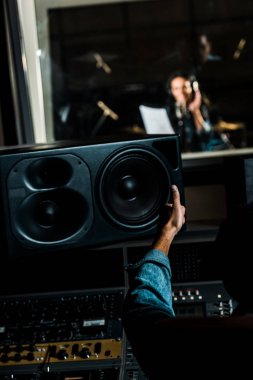 selective focus of mixed race sound producer showing thumb up to woman singing in recording studio clipart