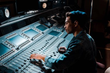 concentrated mixed race sound producer working at mixing console in dark recording studio clipart